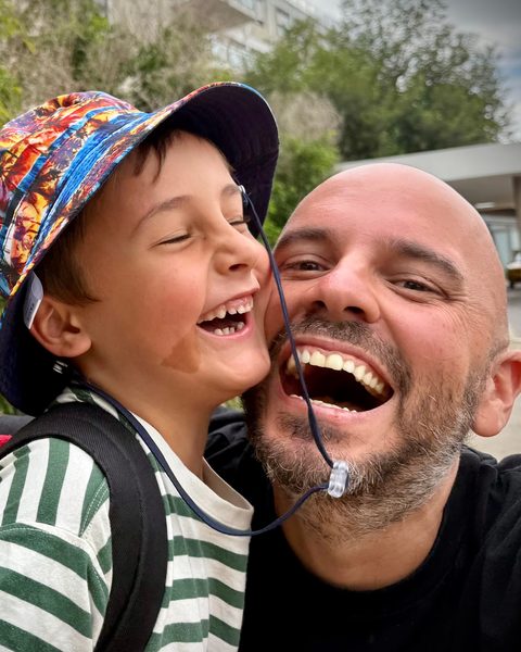 Juan laughing cheek to cheek with Beni, who wears a colourful bucket hat