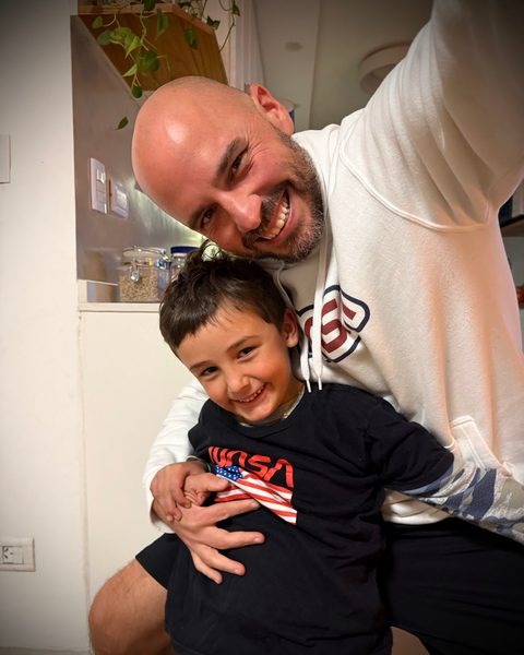 Juan crouching to hug a smiling Beni, who wears a NASA top