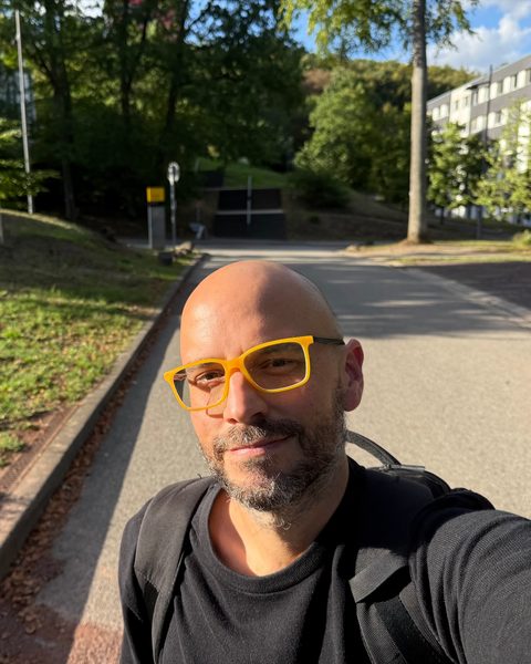 Juan in yellow glasses, taking a selfie on a tree-lined road